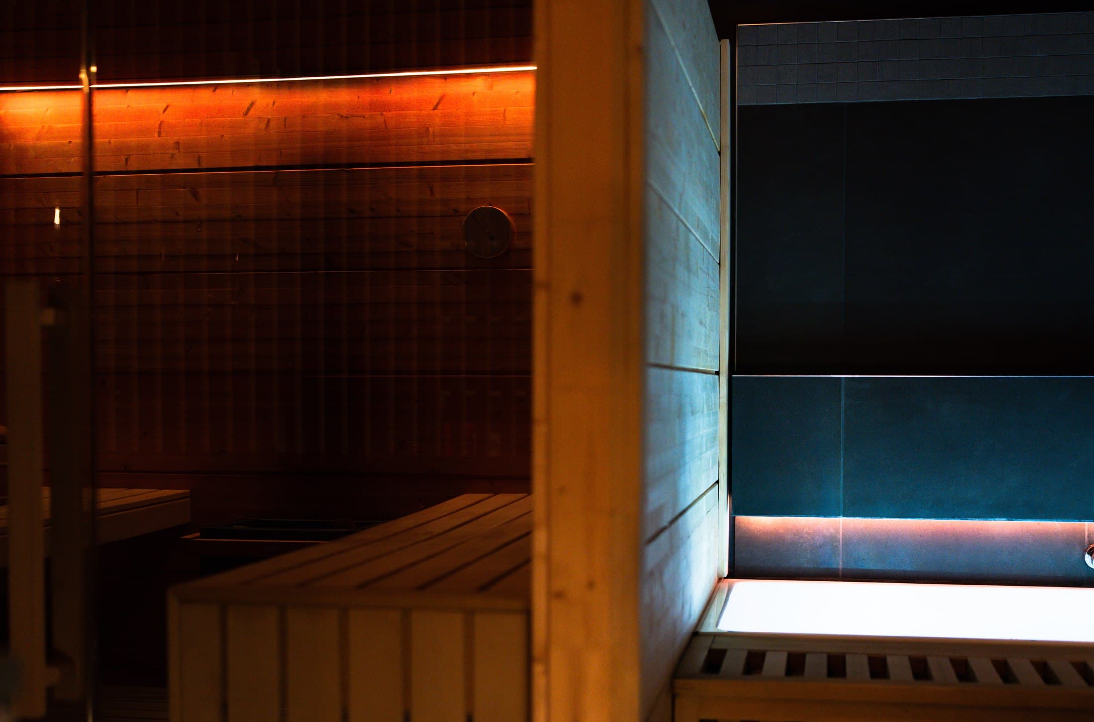 The seam between the cedar sauna and the cold bath, one lit warm, one lit cold